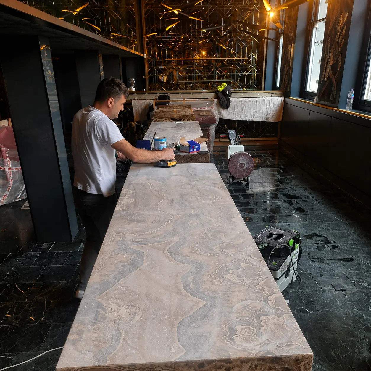 Onyx bar top during restoration, Marius honing the surface with progressive diamond pads in a London hospitality venue