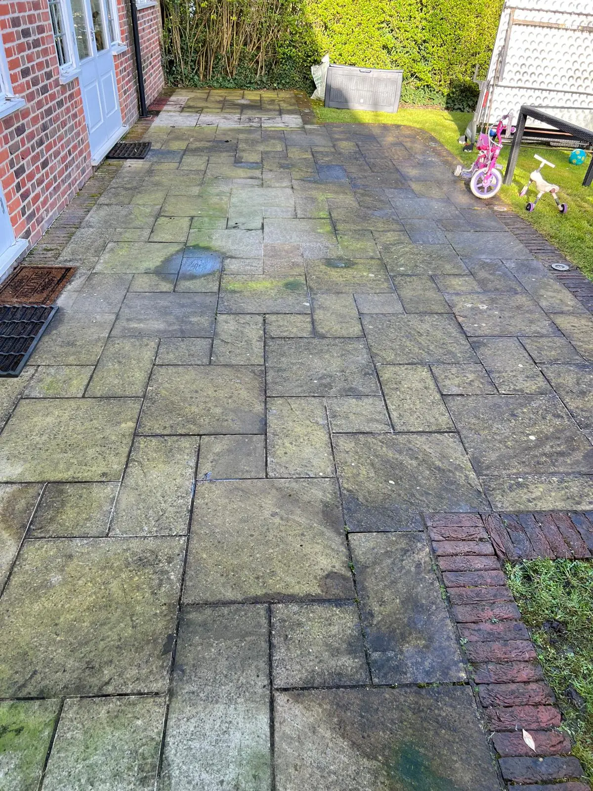 Stone patio before restoration, dirty and weathered slabs with moss and staining, London garden