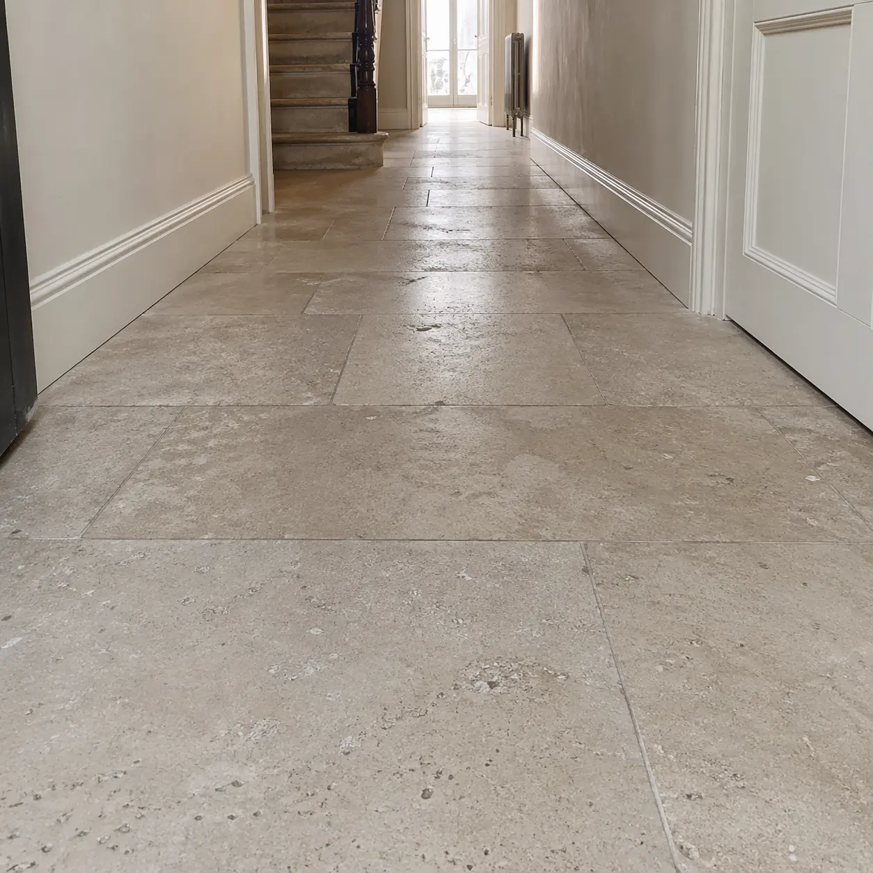 Worn limestone hallway floor before restoration, surface dulled by foot traffic