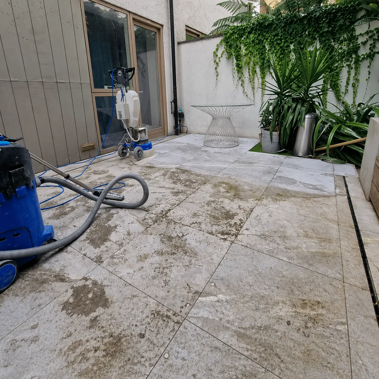 Weathered travertine patio paving with algae, dirt and open voids before restoration
