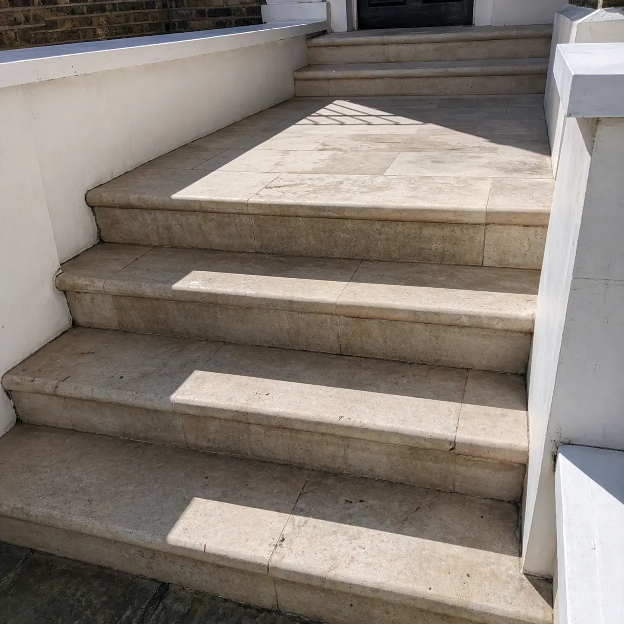 Weathered travertine entrance stairs before restoration, surface darkened and voids open